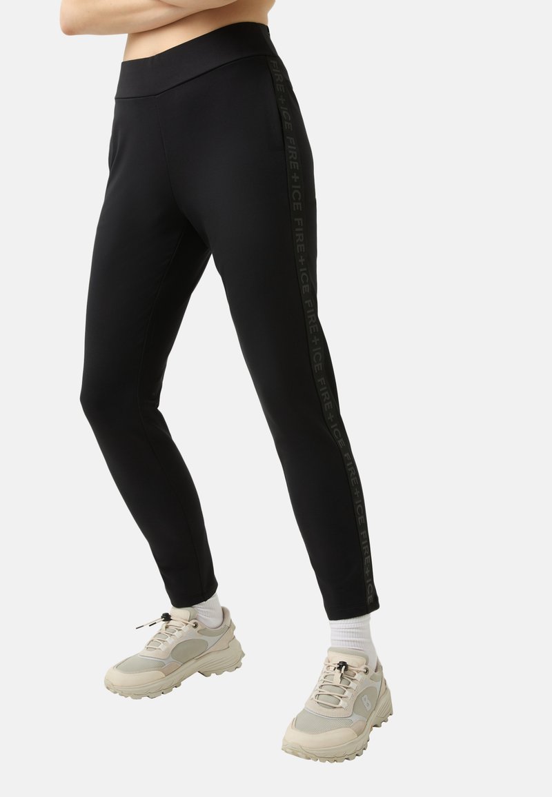 Zwarte leggings van rekbare stof, met een hoge tailleband en een verticale logo-opdruk aan de zijkant. Gemaakt met beige sneakers.