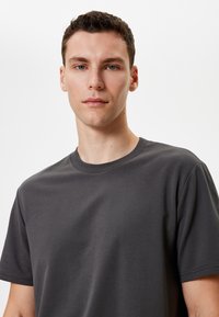 Camiseta de algodón gris con cuello redondo y mangas cortas, que presenta una textura suave y un ajuste relajado. Sin patrones ni acentos visibles.
