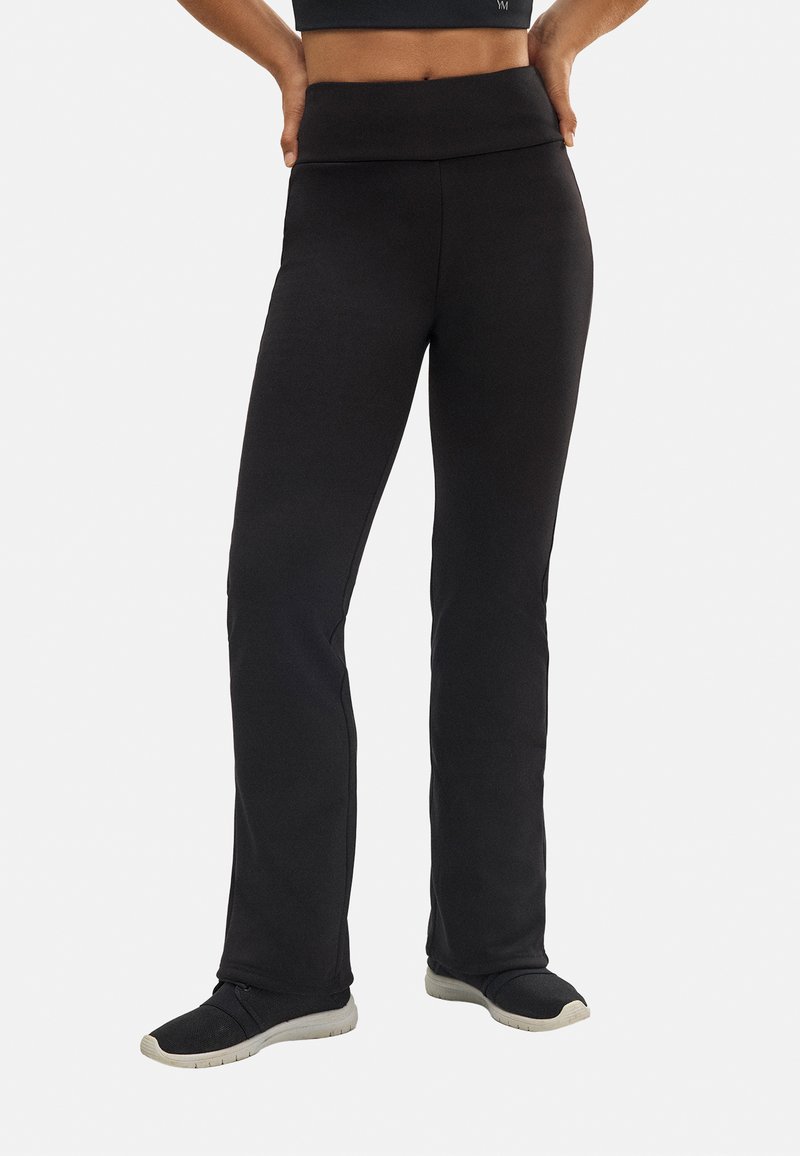 Pantalones deportivos negros, elásticos, con una cintura alta, piernas acampanadas y una textura suave. Adecuados para hacer ejercicio o para uso casual.