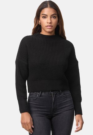 Zwarte cropped trui met een gestructureerd breipatroon, voorzien van een ribbelkraag en -manchetten. Gestyled met donkere jeans in een slim-fit silhouette.