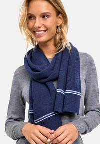 Sciarpa lavorata a maglia di colore blu navy con una texture a coste, caratterizzata da due strisce bianche e azzurro chiaro. La sciarpa è appoggiata intorno al collo.