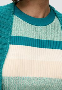 Türkise Strickjacke über einem gestreiften Oberteil in Türkis, Creme und Minze. Das Oberteil zeichnet sich durch eine gerippte Textur und Muster mit kontrastierenden horizontalen Streifen aus.