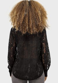 Zwarte kant blouse met lange mouwen, voorzien van een bloemenpatroon, knoopmanchetten en een semi-doorzichtige textuur, gezien van achteren.