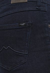 Mörkblå denimjeans med en distinkt bakfickdesign med zigzagstygn, en läderetikett och en liten tyglogodetalj.