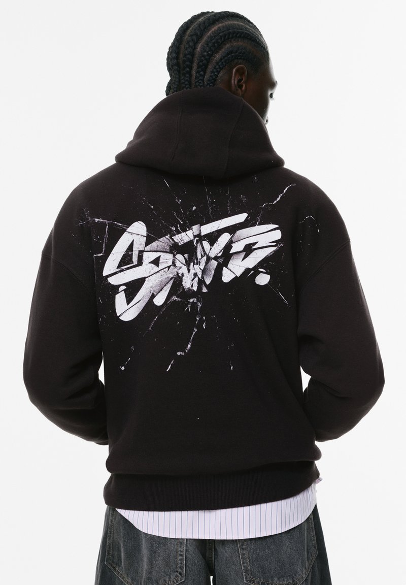 Felpa nera con un grande stampo bianco in stile graffiti sul retro, caratterizzato da un design splatter. Realizzata in un morbido tessuto testurizzato.
