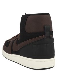 Vysoké tenisky s kombinací hnědé kůže a černé tkaniny. Texturované detaily, bílá mezipodešev a logo na patě.