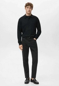 Polo negra de manga larga, con cuello abotonado, combinada con jeans oscuros y zapatos negros. Diseño sencillo con una silueta ajustada.