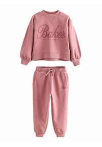 Rožinė sportinė palaidinė ir kelnių komplektas su "Baker by Ted Baker" ženklu, kuris turi elastinius rankogalius ir liemenį, o kelnių juostoje yra raištelis.