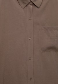 Smeđi button-up košulja s oštrim ovratnikom i jednim džepom na desnoj strani.