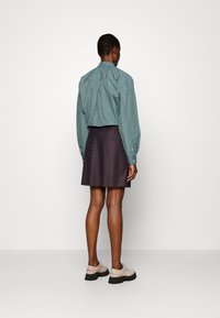 Camicia a righe verdi con maniche lunghe, abbinata a una gonna corta scura. Scarpe chiare con suola spessa completano l'outfit.