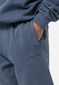 Námornické modré tepláky s hladkou texturou, elastickým pasem, bočními kapsami a vyšitým logem "PGA GOLF" na stehně.