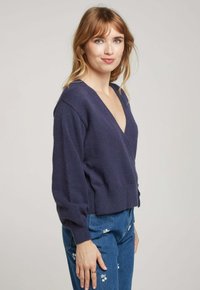Pull en maille bleu marine avec un décolleté en V profond, manches longues et ourlet côtelé. Texture douce avec une coupe décontractée.
