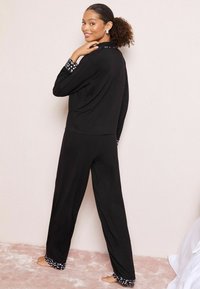 Černý loungewear set s dlouhými rukávy a kalhotami, s puntíkovými akcenty na manžetách. Měkká látka, volný střih a minimalistický design.