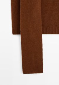 Manche et ourlet en tissu tricot côtelé marron d'un pull sur fond blanc, montrant la texture et le détail du tricot.
