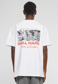 T-shirt en coton blanc avec une impression graphique au dos, portant le texte "BALL HARD" en rouge, et des danseurs dans une photo en noir et blanc au-dessus.