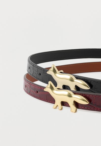 Δύο υφασμάτινες ζώνες από δέρμα, μία μαύρη και μία μπορντό, κάθε μία με μια χρυσή αγκράφα σε σχήμα αλεπούς, τοποθετημένες σε σπείρα πάνω σε άσπρο φόντο.