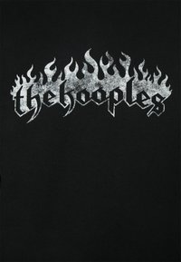Svart t-shirt med en metallisk silverfärgade låga grafik ovanför texten "thehooples" i en fet, stiliserad font. Mjuk bomullsmaterial.