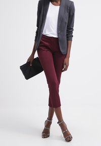 Šedý blazer, bílý tričko a burgundské cropped kalhoty. Černá kabelka na ruku a stříbrné sandály na podpatku. Hladké textury a přizpůsobený střih.