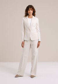 Valge kohandatud bleiser ühe nupuga, kombineeritud laiade bretspükstega. Sile kangas puhta disainiga. Allosas lihtsa ümmarguse kaelusega särk.