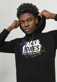 Sudadera negra con una impresión gráfica en la parte frontal. Presenta una capucha con cordón y un bolsillo tipo canguro. El texto incluye "JACK & LONES" en blanco negrita.