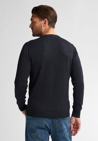 Ciemnoniebieski sweter z dzianiny z długimi rękawami i okrągłym dekoltem, w połączeniu z niebieskimi dżinsami. Materiał wydaje się gładki i dopasowany.