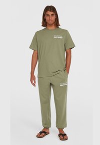 Camiseta de algodón verde olivo con mangas cortas y el texto "La Sociedad de Surf del Futuro", acompañada de unos joggers a juego con bajos ajustados.