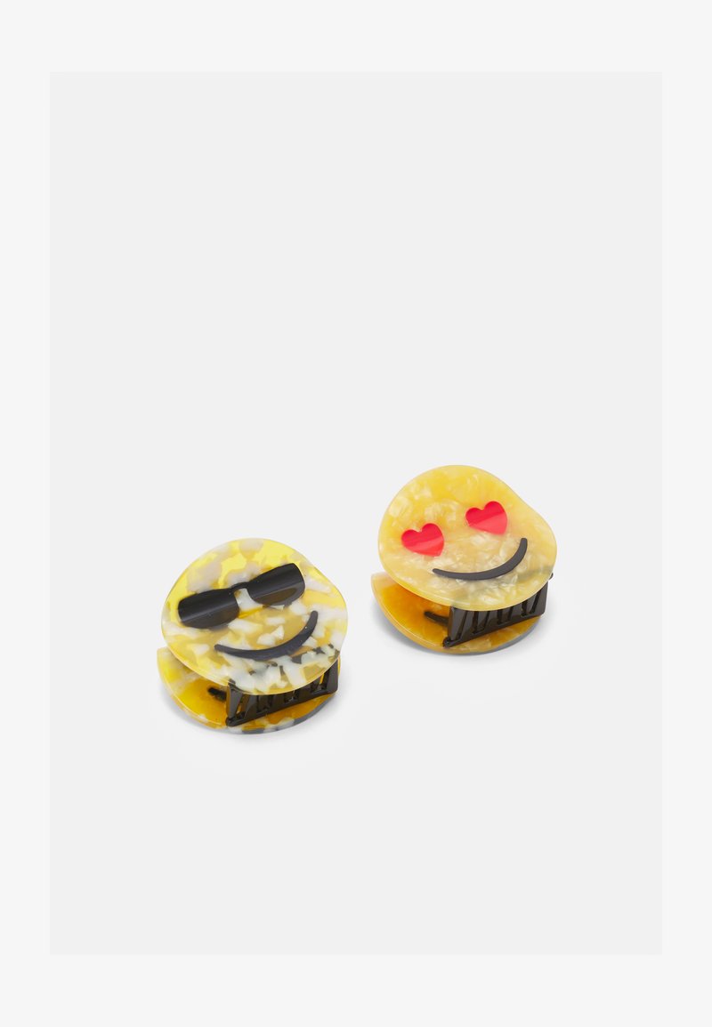 Pregadores de cabelo em forma de emoji amarelo com um acabamento brilhante. Um pregador tem óculos escuros pretos, e o outro tem olhos de coração, ambos com hardware preto.