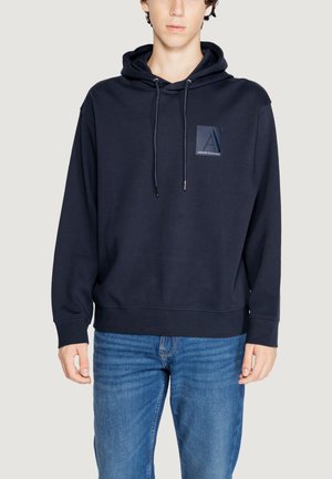 Sudadera azul marino hecha de una tela suave, con un bolsillo frontal y capucha con cordón. Incluye un parche de logo de marca en el pecho.