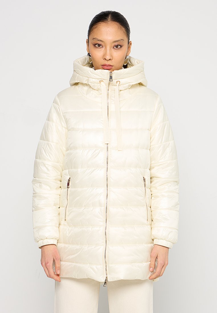 Giacca puffer color crema con cappuccio, chiusura a zip e tasche laterali. Presenta un design trapuntato e una texture leggera e liscia.