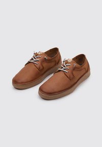 Zapatos de cuero marrón perforados con cordones gris claro, punta redondeada y suela de goma color beige. Presentan un detallado de costura y una superficie texturizada.