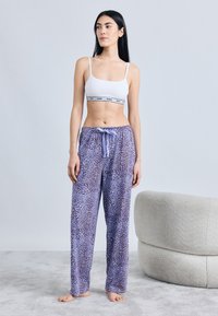 Ærmeløs hvid crop-top med sort bånd, kombineret med lilla pyjamasbukser med leopardprint, der har snøre i taljen og løs pasform.