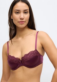 Bordó párnázott melltartó csipkés díszítéssel a tetején, állítható szatén pántokkal és sima kivitelben. Középen díszes masnival.
