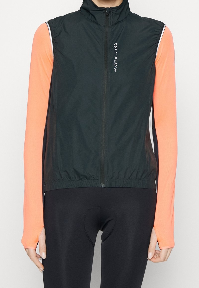 Black lightweight zip-up vest with high collar, elastic hem, and white logo. Worn over a long-sleeve, bright orange athletic top.