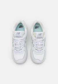 Weiße Ledersneaker mit Mesh-Akzenten, die blaue Details, einen gepolsterten Kragen und ein klassisches Schnürdesign aufweisen. Modell 574 von New Balance.