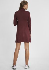 Robe bordeaux à manches longues avec un col haut, en tissu doux, présentant une coupe décontractée et un design d'ourlet légèrement évasé.