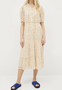 Luftig midiklänning i ljusbeige med blommönster. Puffärmar, gatherad midja, lagerkjol. Matchad med blå mockasandaler.