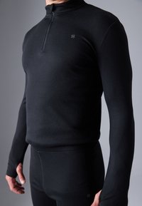 Melnā sporta krekls ar ceturtdaļas rāvējslēdzēju, pieguļošs dizains, garas piedurknes, gluda tekstūra un logotips uz krūtīm.