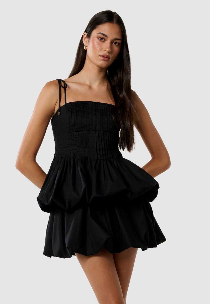 Robe noire avec un corsage sans bretelles ajusté et une jupe évasée à volants. Présente une texture plissée et des bretelles ajustables. Tissu lisse.