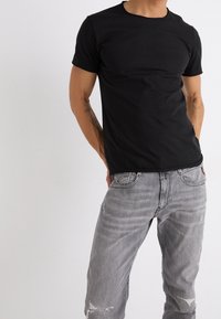 Camiseta de algodón negra con cuello redondo y mangas cortas, combinada con unos jeans de mezclilla gris desgastados que presentan desvanecidos y desgastes.
