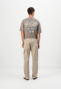 Gray t-shirt with printed graphics on the back, paired with beige cargo pants featuring multiple pockets and a straight-leg design.