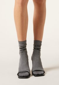 Calzini grigi scintillanti con una trama a coste, arricciati nella parte superiore, caratterizzati da un design nero con punta aperta e tacco quadrato.