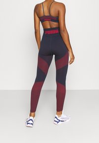 Conjunto deportivo en azul marino y burdeos que incluye un sujetador deportivo con tirantes finos y leggings de cintura alta con paneles texturizados y acentos con el logo de PUMA.