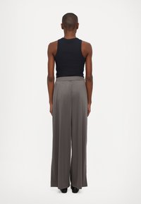 Top senza maniche nero e pantaloni grigi ampi e larghi, caratterizzati da una vita elasticizzata e una texture di stoffa liscia, visti da dietro.