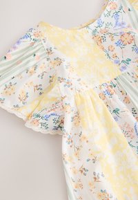 Blumenkleid mit gelben und weißen Mustern, grünen und weißen Streifen, Rüschenärmeln und Spitzenbesatz am Saum. Baumwollmaterial.