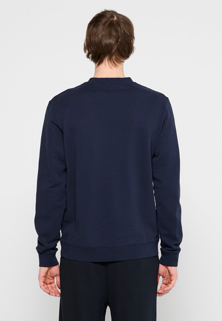 Marineblauwe ribbeltrui met lange mouwen en een ronde halslijn. Heeft een effen achterkant en een aansluitende tailleband. Geen zichtbare patronen of accenten.