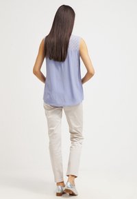 Top senza maniche azzurro chiaro con dettaglio in pizzo sulla schiena, abbinato a pantaloni beige chiaro e scarpe argentate, visto da dietro.