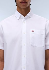 Weißes Kurzarmhemd aus Baumwolle mit Button-Down-Kragen, ausgestattet mit einer Brusttasche und einer kleinen norwegischen Flagge, die darauf gestickt ist.