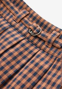 Close-up of a brown and black checkered fabric belt with a silver double-ring buckle threaded through belt loops.