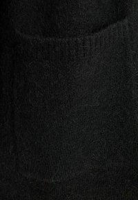 Gros plan d'un tissu en laine noire douce avec un détail de texture côtelée près du bord supérieur, montrant des fibres fines et un motif de tricot.