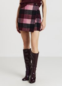 Minigonna a quadri in tonalità di rosa e nero, con design avvolgente e dettaglio con bottone. Abbinata a stivali bordeaux al ginocchio.
